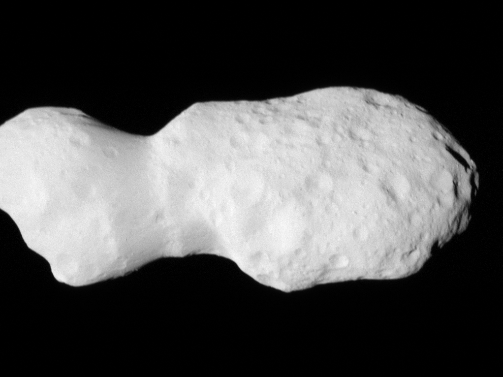 Gif of Asteroid Donaldjohanson, as seen by the Lucy spacecraft during its close flyby. The asteroid looks like two lobes, attached by a thinner cylinder, like a barbell with very large weights. One lobe is smaller than the other. Although they are both about the same circumference, the smaller lobe is less wide than the other. The asteroid is a smooth, light gray surface, with smooth-edged craters dimpling its surface. The larger lobe has many more craters. The asteroid moves closer to the camera, pushing in on the larger lobe. Then it rotates slightly to look along the asteroid long-ways.