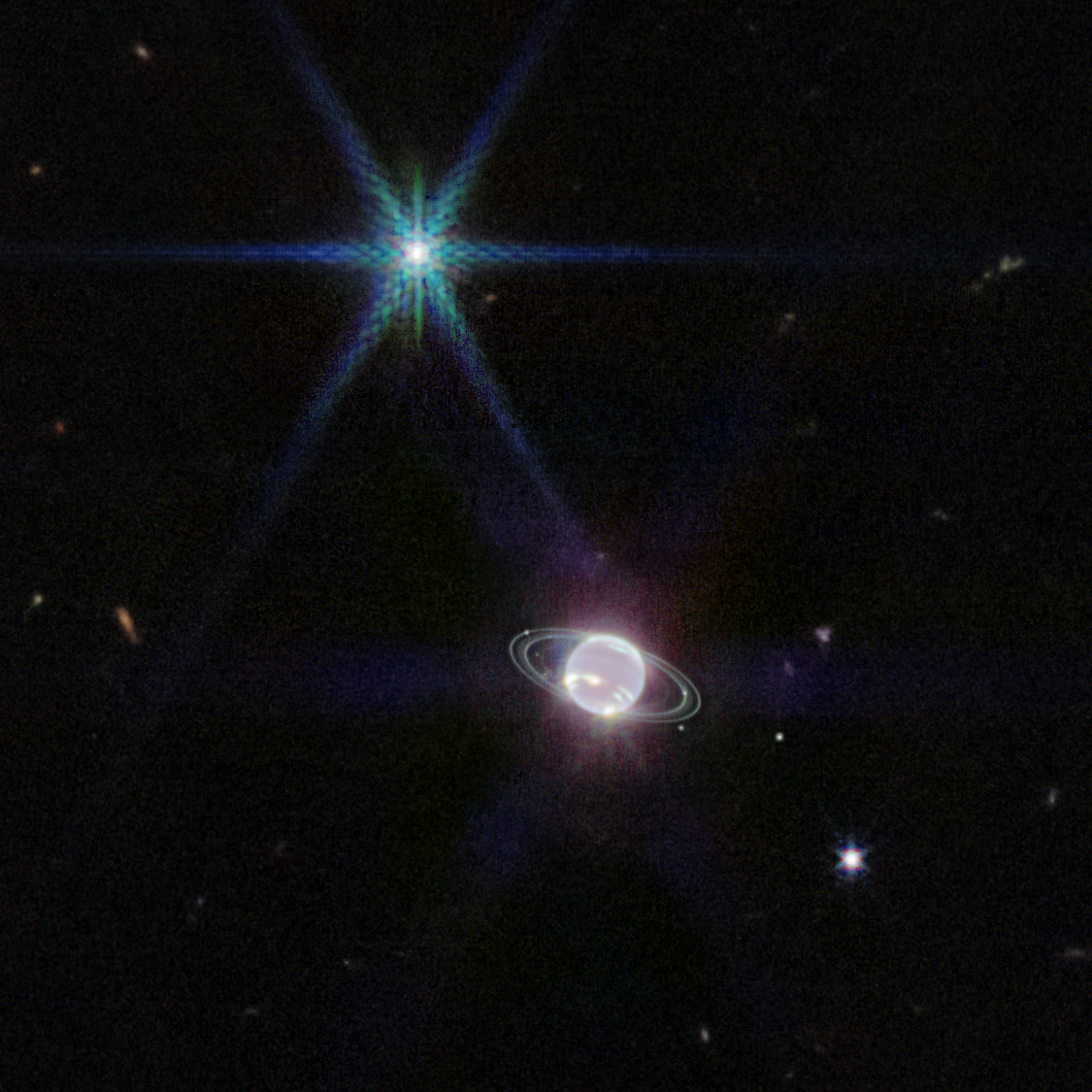 This distant view of Neptune shows the planet as small, shiny orb surrounded by faint rings with stars and galaxies in the background.