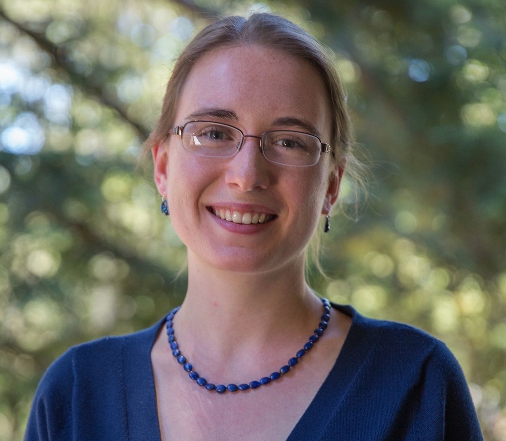 Portrait photo of a smiling woman standing outside with a tree behind her