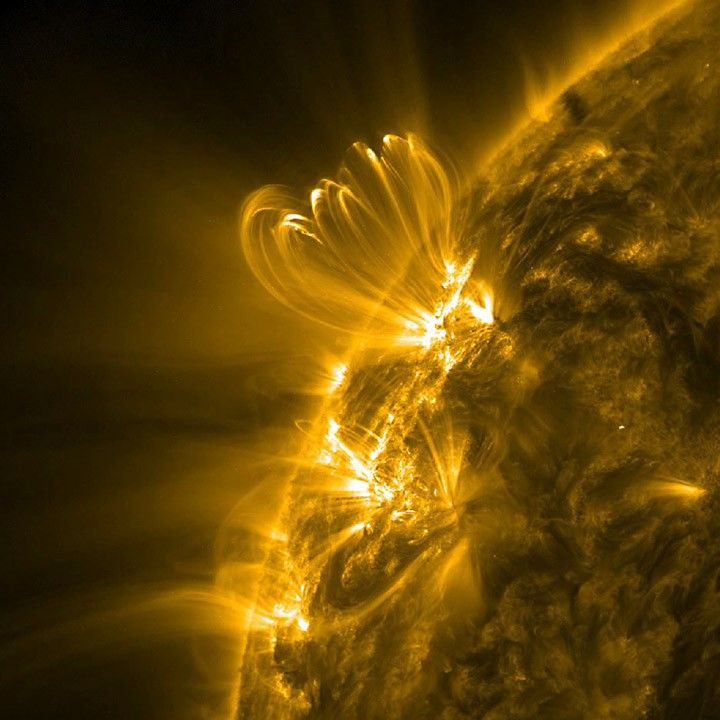 A portion of the Sun appears in shades of gold and black. In the upper left, several gold-shaded arches rise above a bright region on the Sun.