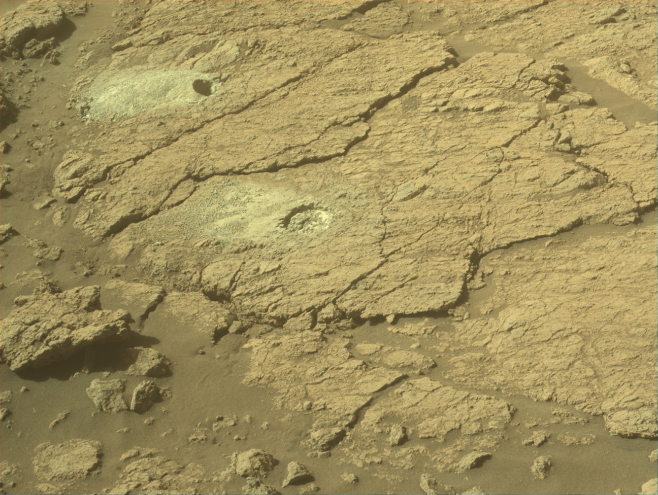 A circular drill hole with a pile of dust next to it on the surface of Mars.